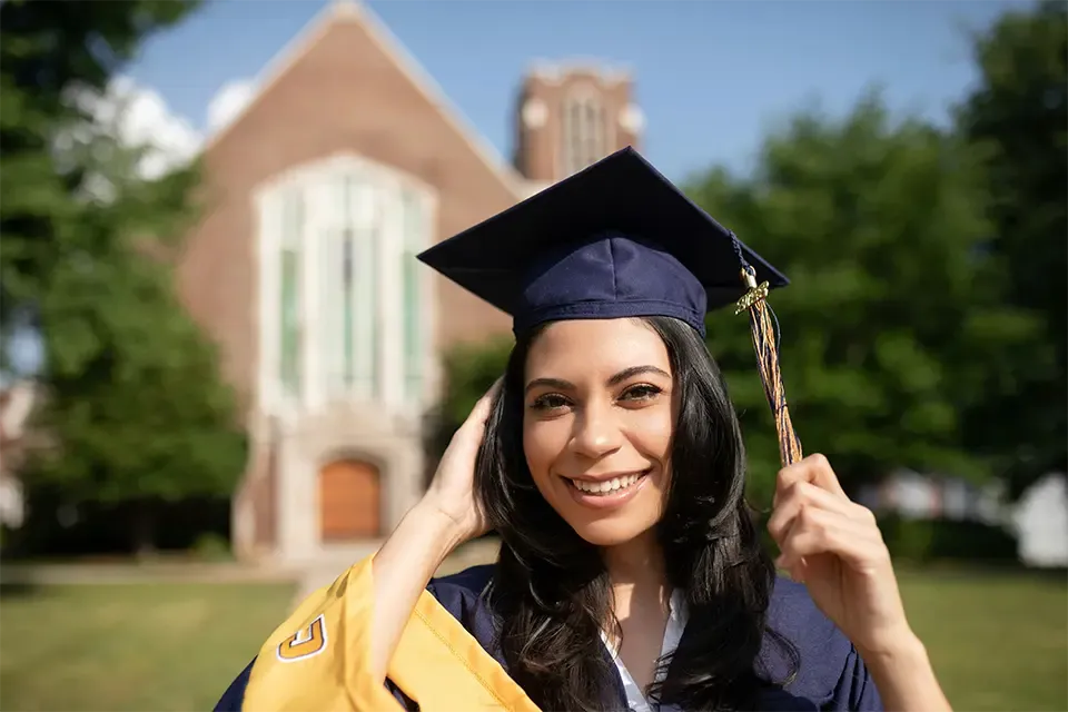 young woman wearing graduation gown and cap at her college graduation ceremony